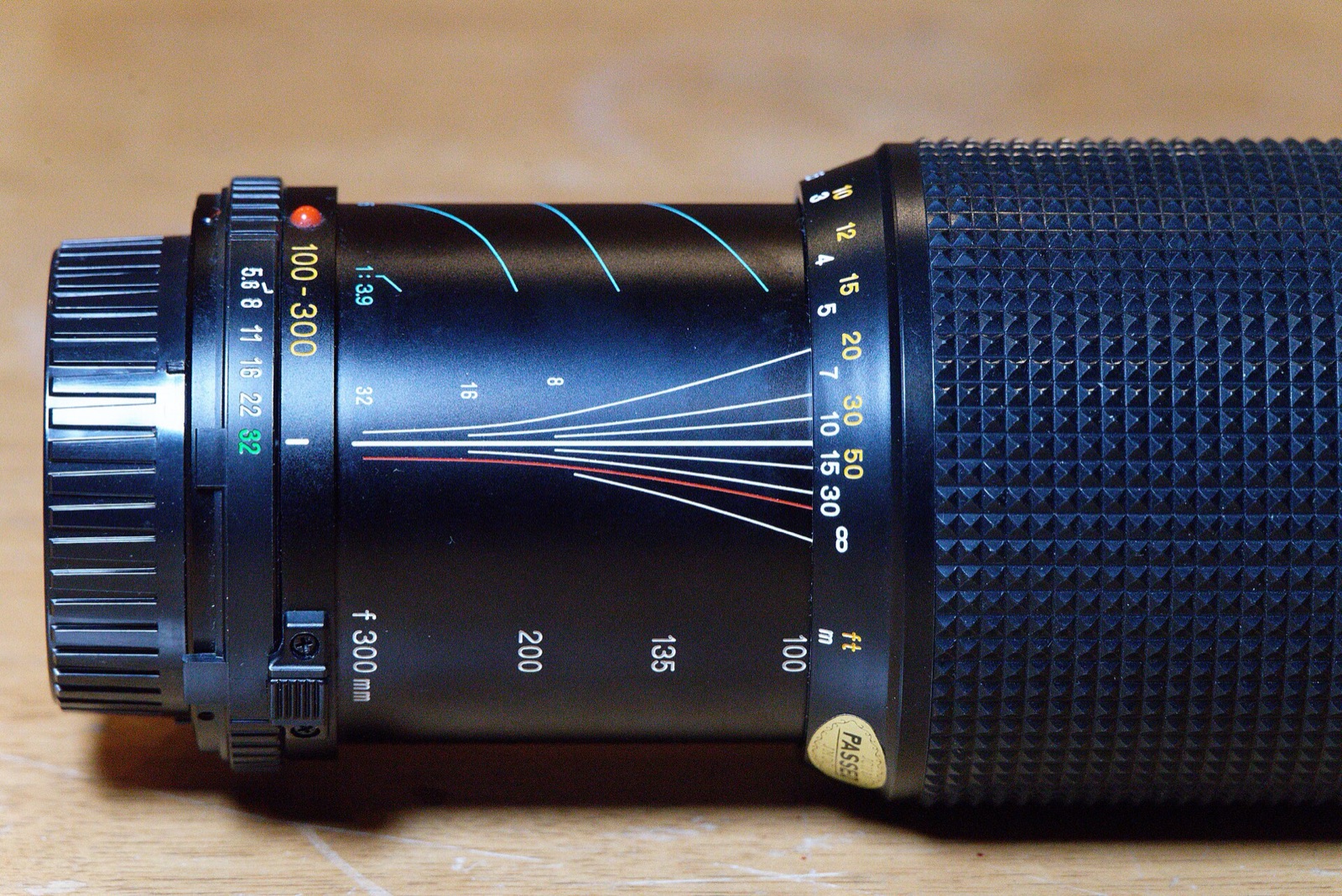 Side view of a zoom lens barrel with curved coloured depth-of-field lines engraved along it.