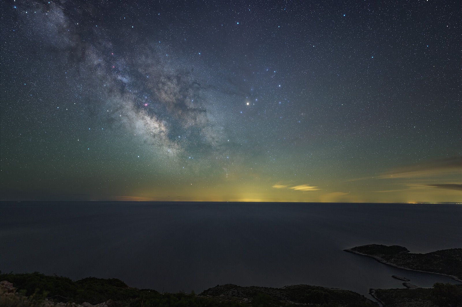 Milky Way over the sea at night with distant city light domes glowing on the horizon