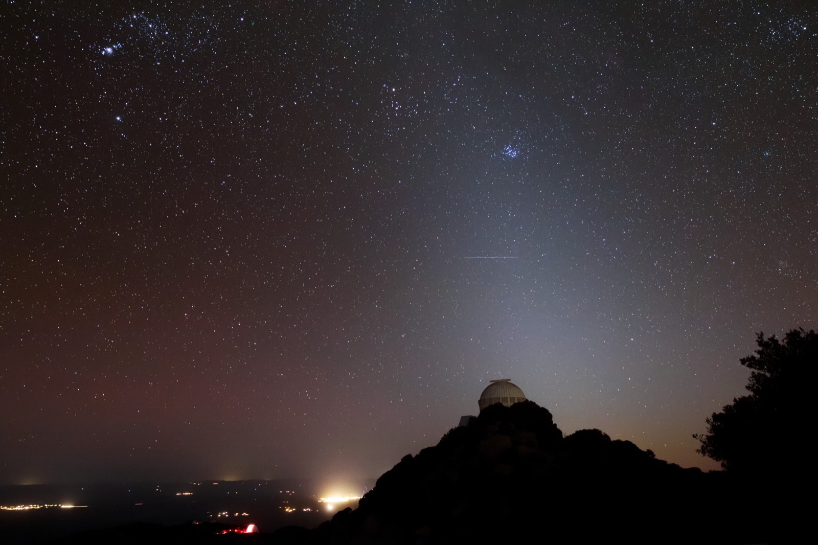 Observatory domes under stars with the orange light dome of a city on the horizon