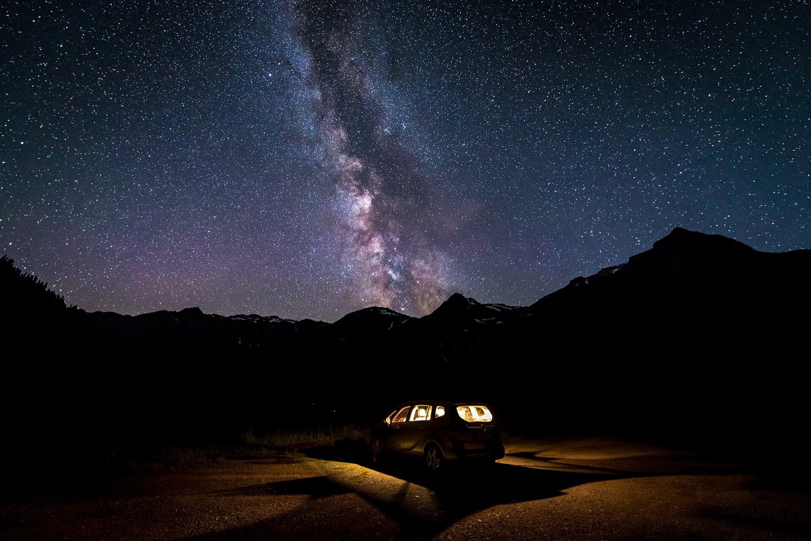Milky Way above mountains with the foreground ground lit by a parked car's interior light