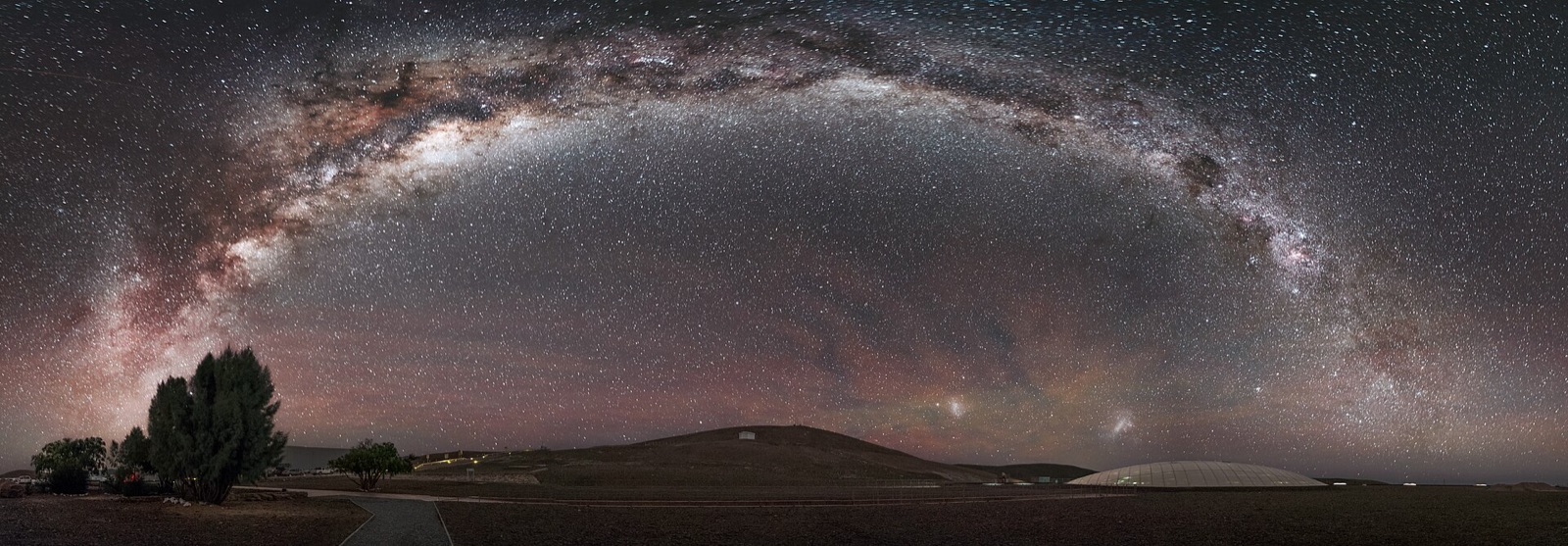 Milky Way arch over a desert with a glass dome in the foreground and green and red airglow.