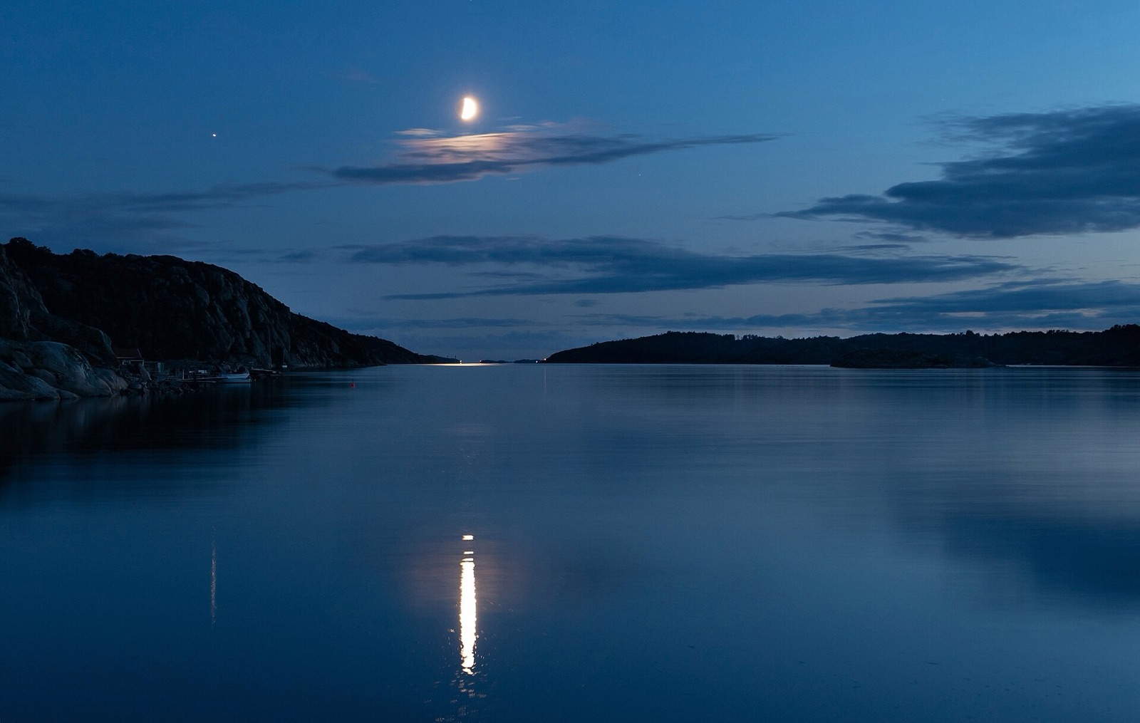 Half Moon over a calm fjord at dusk with a bright reflection path on the water.