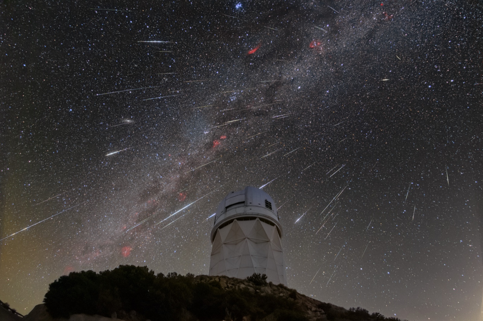 Several meteors streaking across a starry sky with the Milky Way above an observatory dome