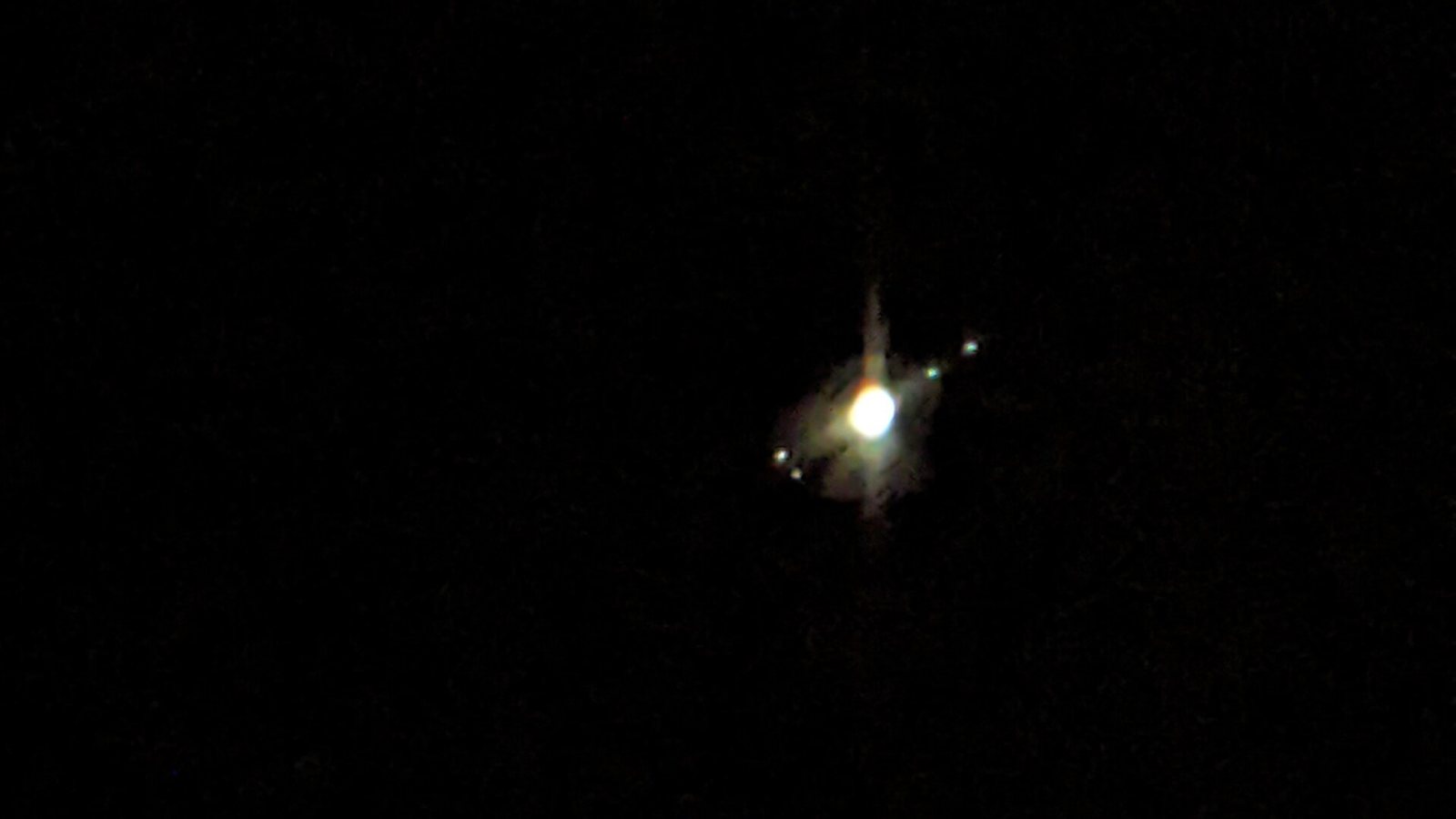Jupiter as a bright disc with four small moons lined up beside it