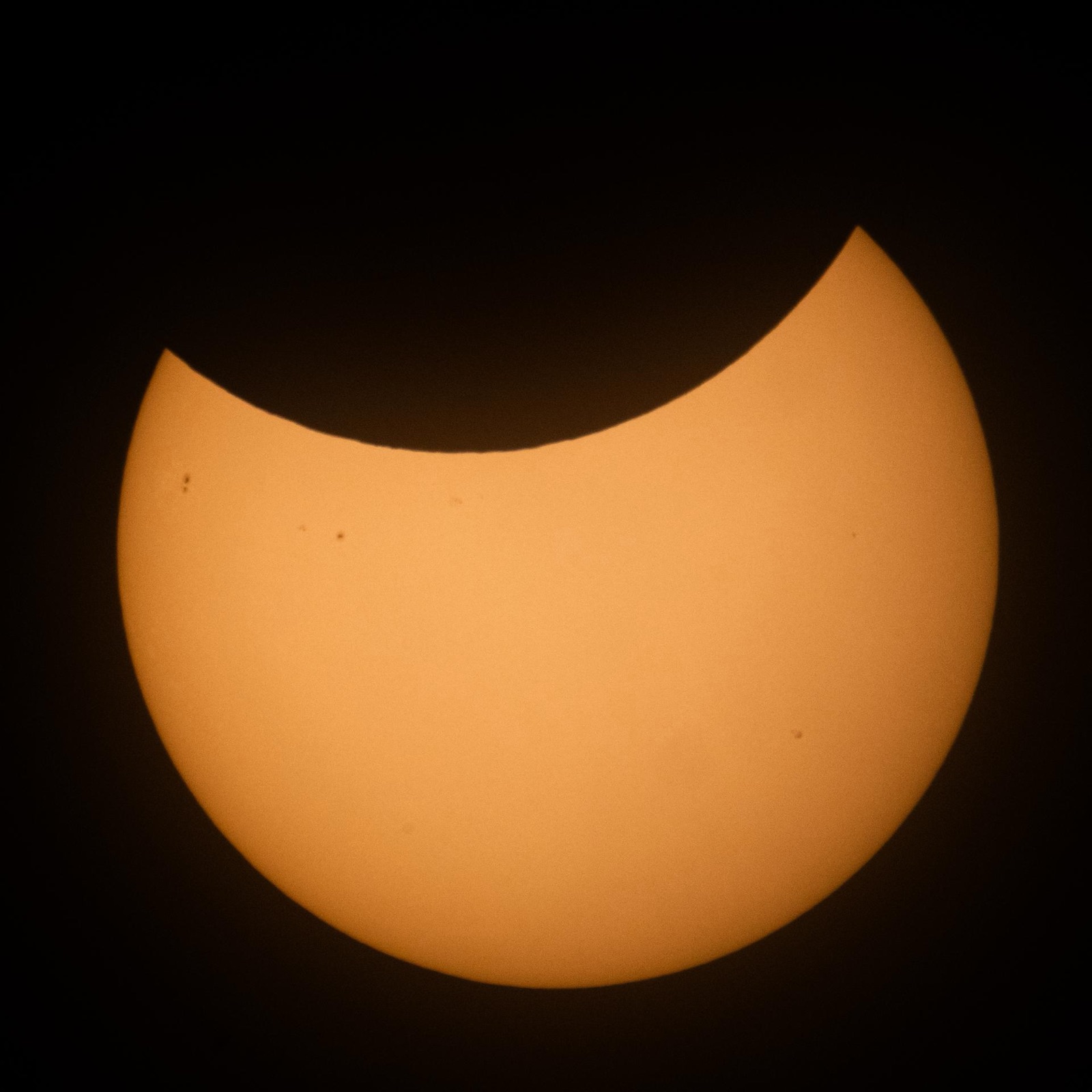 Orange Sun with a large curved bite taken from its upper edge on a black background.