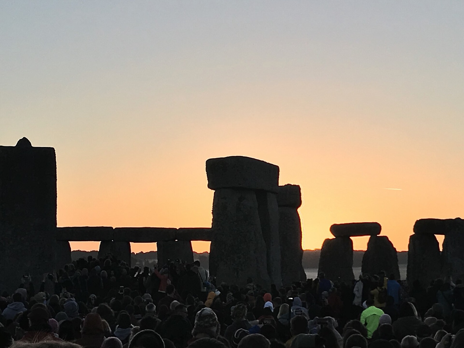 Sun rising between the standing stones of Stonehenge with a silhouetted crowd below.