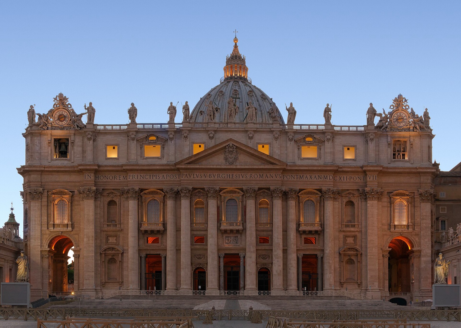 Floodlit facade and dome of St Peter's Basilica under a deep blue dusk sky.