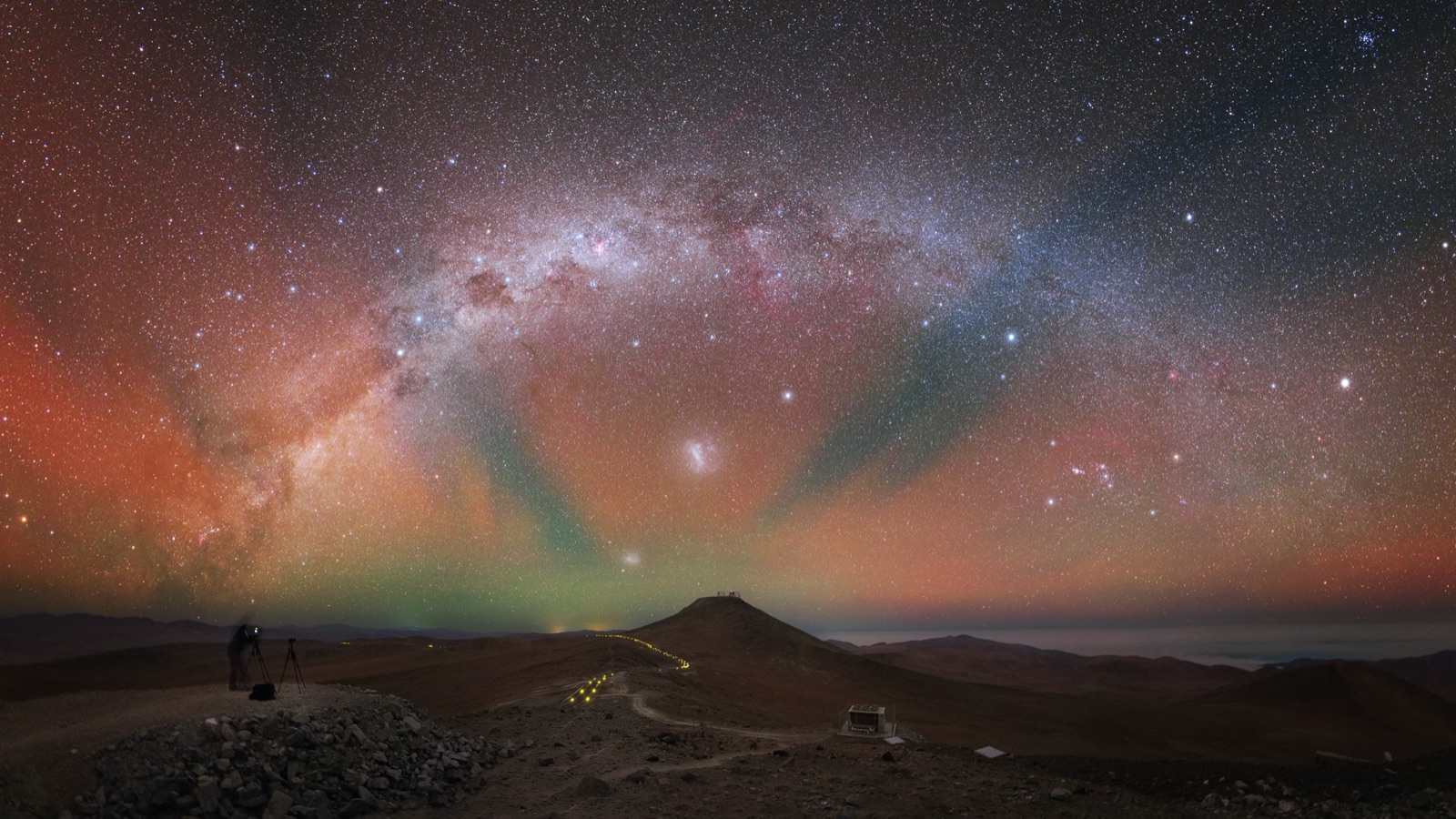 Green and red airglow bands across a starry sky with the Milky Way above a desert observatory